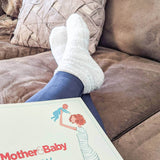 Person wearing white socks and blue leggings with a 'Mother & Baby' magazine on a brown couch. thumbnail
