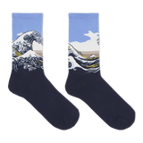 A pair of crew socks featuring a graphic print of Katsushika Hokusai's Great Wave off Kanagawa. The lower half of the socks is a solid dark navy blue, while the upper half features the wave illustration with a light blue sky, white foam, and a tan mountain range. thumbnail