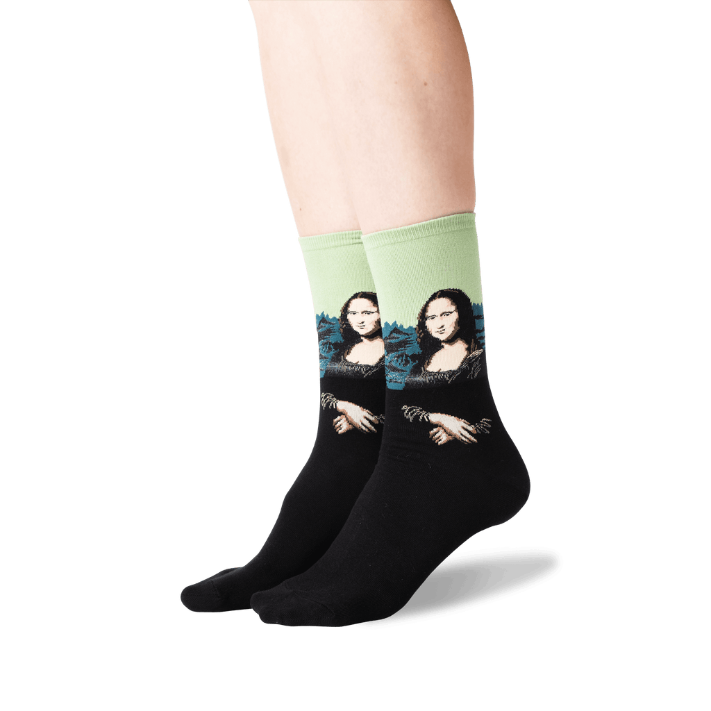 A pair of crew socks worn on a person's feet, featuring a black lower half and a light green upper half with a printed parody of the Mona Lisa wearing sunglasses.