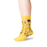 A pair of bright yellow crew socks with a detailed art print of Gustav Klimt's 'The Kiss' on the sides, shown on a person's feet against a plain white background.