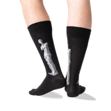 A pair of black crew socks worn on a person's legs, featuring a large white sculpture design on the side of each sock, photographed against a clean white background. thumbnail