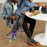 Two people sitting at a table with colorful socks on, one person is reaching into a cauldron.