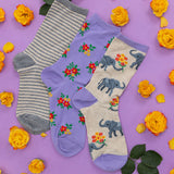 Three pairs of socks with floral and elephant designs on a purple background with yellow flowers. thumbnail