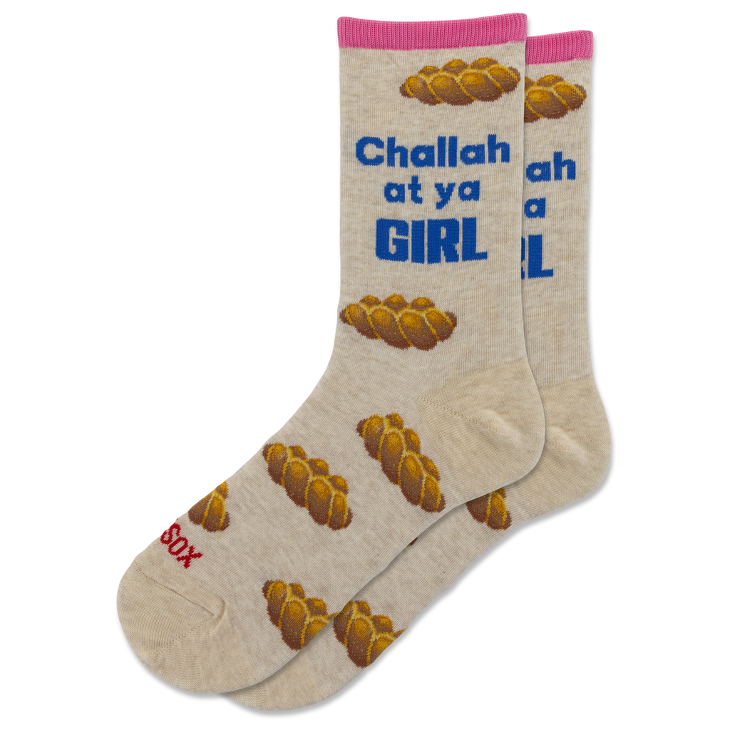 A pair of beige crew socks with a pink cuff, featuring a pattern of braided bread loops and blue text that reads 'Challah at ya GIRL'. One sock also has red text reading 'Sax' near the toe.