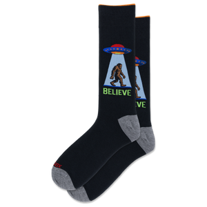 A pair of black crew socks with gray heels and toes, featuring a graphic of a Bigfoot silhouette under a UFO with the word 'BELIEVE' in green.
