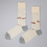 A pair of crew socks with a beige and gray color-blocked design, featuring a printed graphic of two hands reaching toward a crack in the wall, styled on a neutral gray background. thumbnail