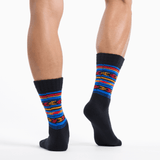 A pair of crew socks worn on a model's legs, featuring a black base with vibrant horizontal stripes in blue, red, orange, and yellow on the upper portion.