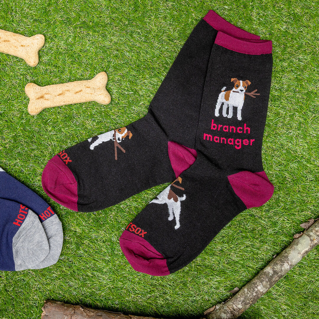 Black socks with dog illustrations and 'branch manager' text on a grass background with dog bones and a branch.