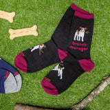 Black socks with dog illustrations and 'branch manager' text on a grass background with dog bones and a branch.