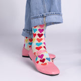 Colorful heart-patterned socks worn with pink shoes and blue jeans on a light gray background
