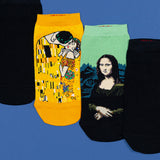 Three novelty ankle socks displayed on a blue background, featuring artwork from Gustav Klimt's 'The Kiss' and Leonardo da Vinci's 'The Mona Lisa' on black socks.