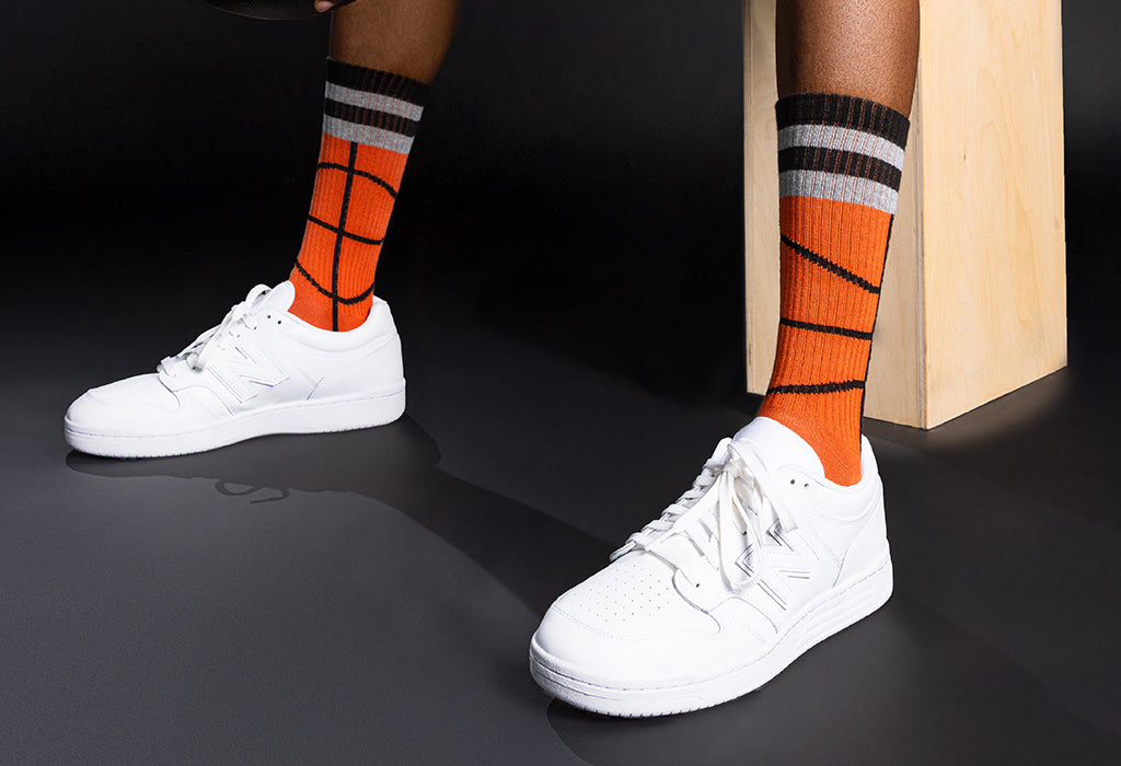 White sneakers with orange and black striped basketball socks on a dark background