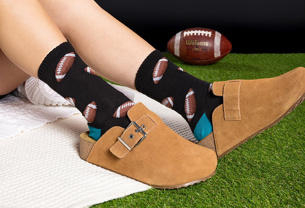Person wearing black socks with football patterns and brown shoes on a grassy surface.
