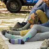 Two people sitting on a camping mat wearing colorful socks with 'Jeep' branding, next to a vehicle and tent. thumbnail