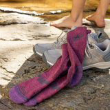 Purple hiking socks with a logo on gray shoes by a stream