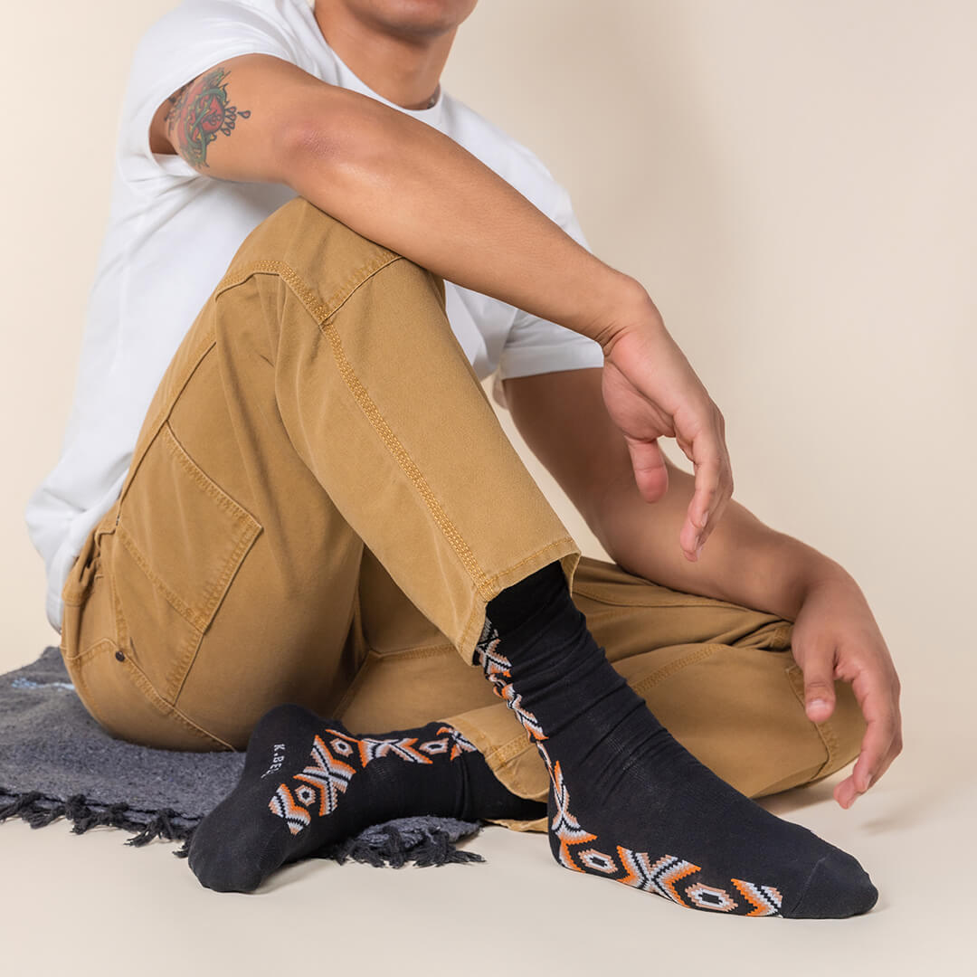 Person wearing black socks with patterned toes and heels, sitting on a beige surface.