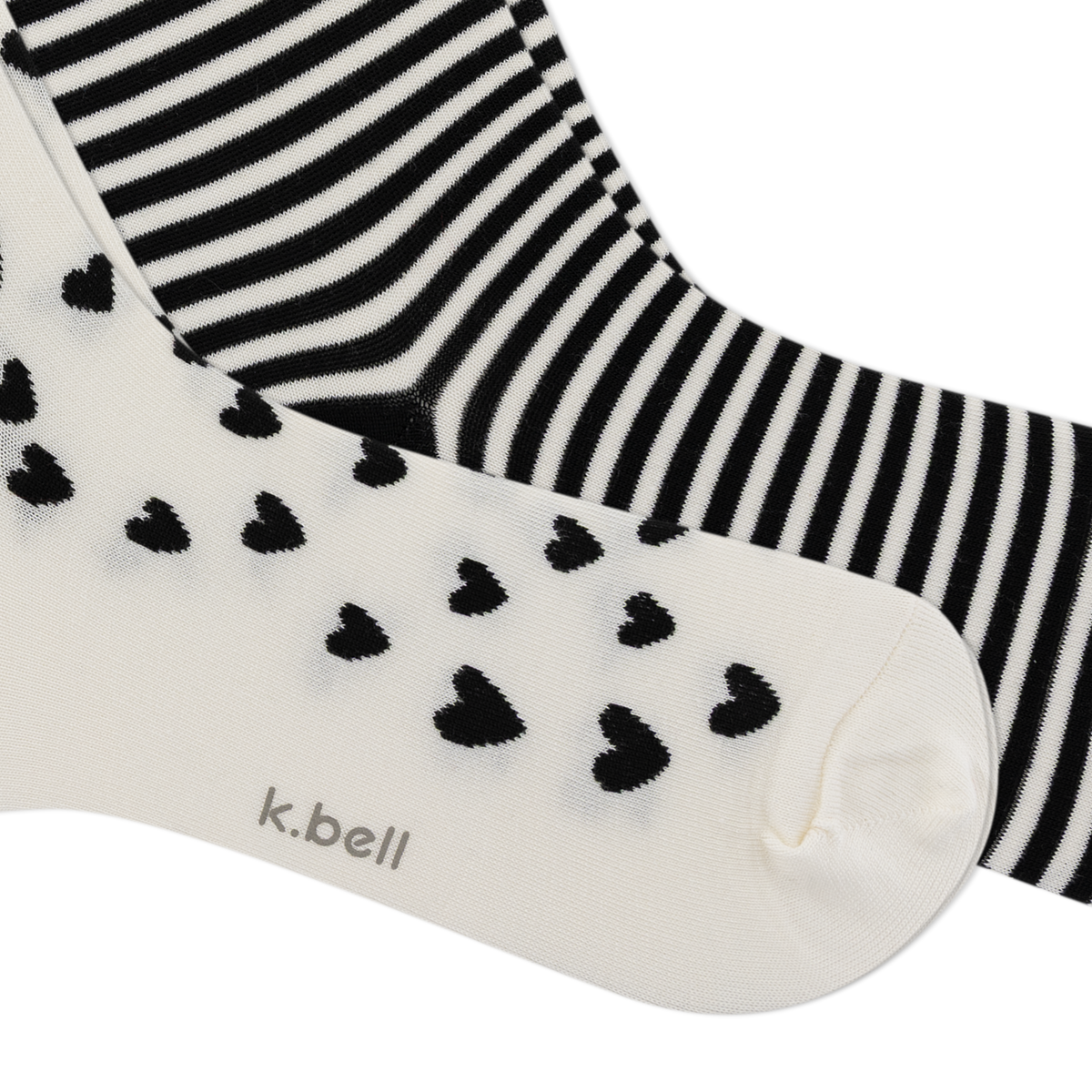 Two pairs of socks from k.bell, one in black and white stripes and the other in off-white with black hearts, shown on a white background.