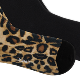 A close-up of a pair of crew socks, with one sock showing a leopard print pattern in beige, brown, and black, and the other sock showing a solid black knit. The brand name 'k.bell' is on the bottom of the foot. thumbnail