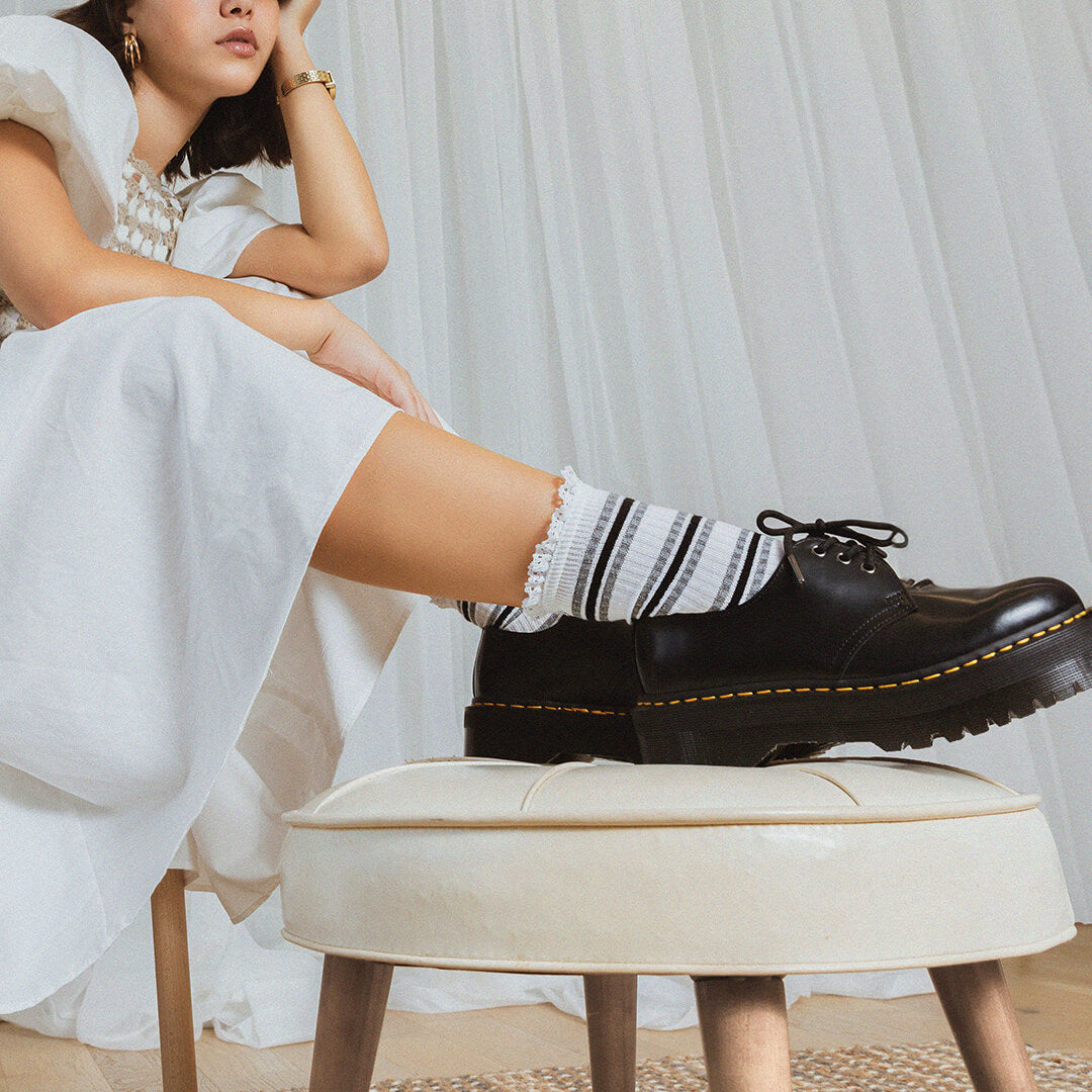 Person wearing black shoes and black and white socks with black stripes sitting on a stool.