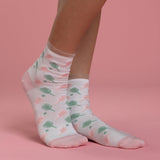 White socks with green and pink pickleball patterns worn by a person on a pink background