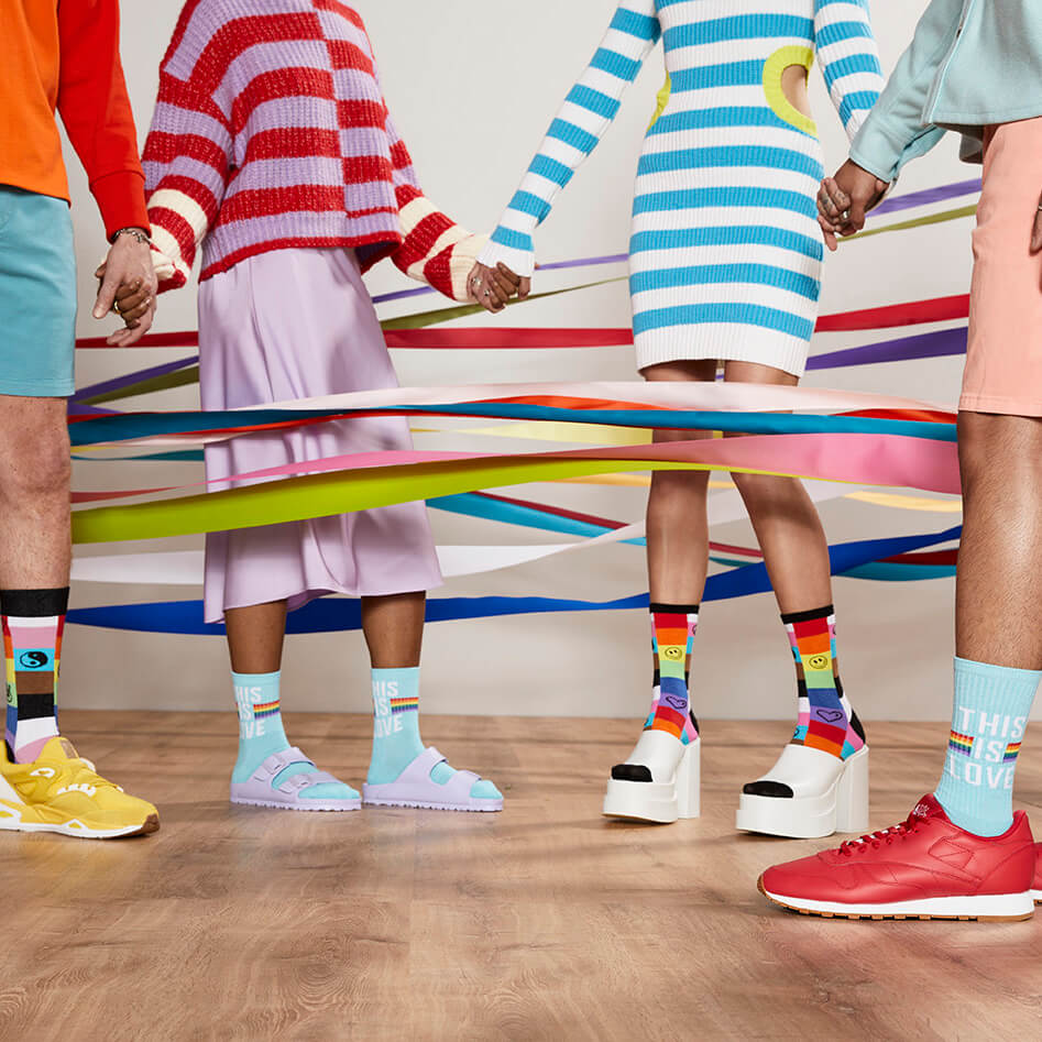 Group of people in bright colored clothes surrounded by ribbons wearing pride-themed socks.