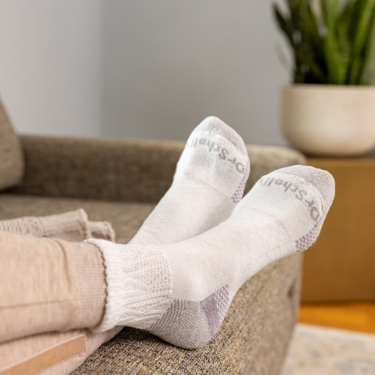 Person wearing white socks with text, sitting on a couch in a home setting.