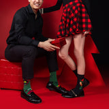 Man and woman on a red background wearing festive socks and shoes.