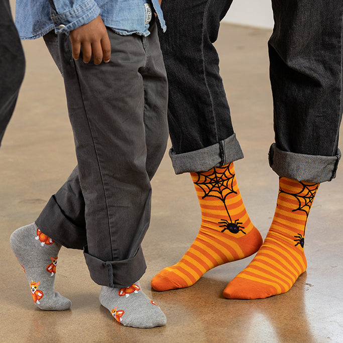 Two pairs of feet wearing Halloween-themed socks on a neutral background
