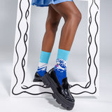 Person wearing blue socks with Hokusai's 'The Wave' pattern and black shoes on a plain background thumbnail