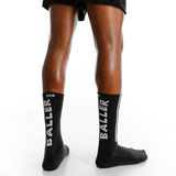 Black socks with 'BALLER' branding worn by a person on a white background thumbnail