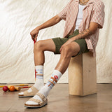 Person sitting on a wooden block wearing striped socks with colorful patterns, surrounded by croquet equipment. thumbnail