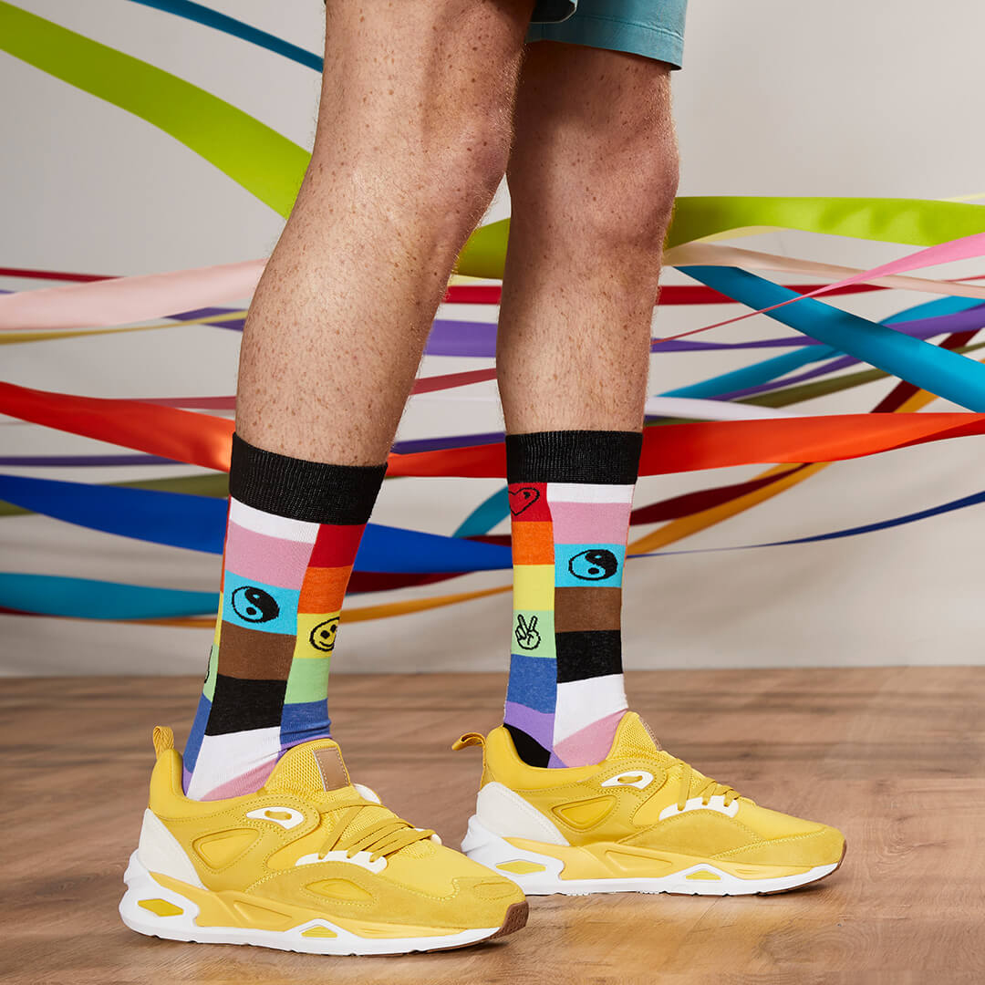 Person wearing colorful socks with a pattern and yellow sneakers on a wooden floor.