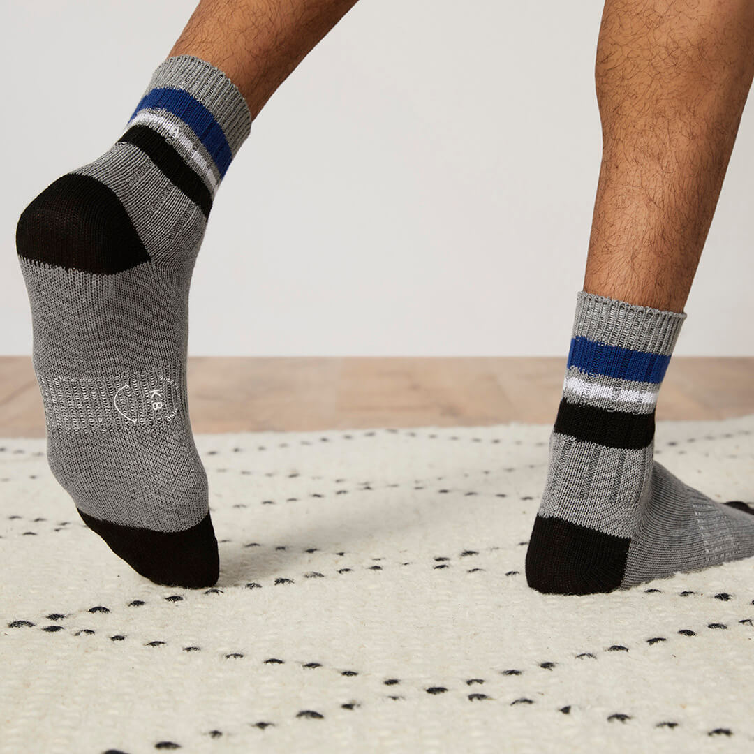 Gray socks with black toes and blue stripes worn by a person on a light wooden floor.
