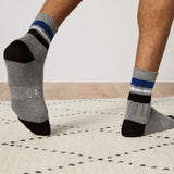 Gray socks with black toes and blue stripes worn by a person on a light wooden floor.
