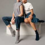 Two people sitting on a white stool wearing gray and black socks against a gray background thumbnail