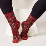 Red socks with black and white pattern worn by a person sitting on a white stool. thumbnail
