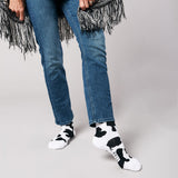 Person wearing blue jeans and cow print socks on a plain background