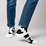 Person wearing black and white cow print socks with 'K-Bell' branding, paired with blue jeans on a gray background. thumbnail