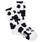 A pair of white crew socks with black cow print and the brand name 'K.BELL' written across the foot.