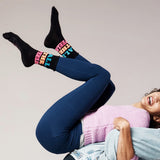 Person wearing colorful socks with text, blue leggings, and a pink sweater against a plain background thumbnail