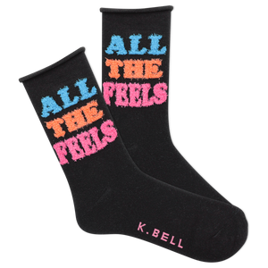 A pair of black fuzzy socks with the text 'All The Feels' in blue and pink colors, and the brand name 'K.Bell' at the end of the foot.