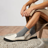 Person wearing white loafers and gray socks sitting on a textured surface. thumbnail