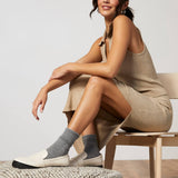 Woman sitting on a chair wearing a beige dress and gray socks with white shoes. thumbnail