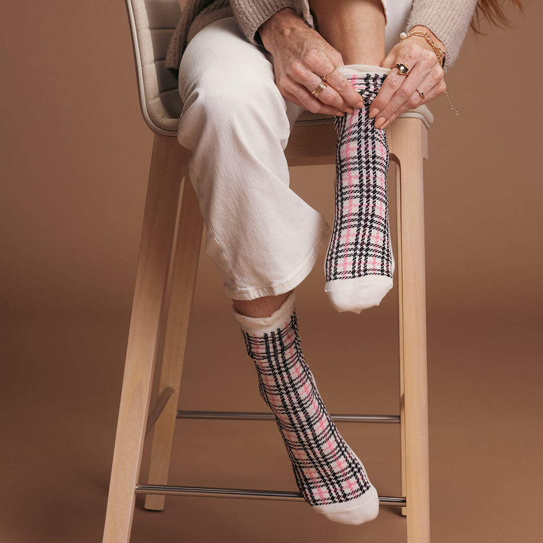 Person sitting on a stool wearing pink plaid socks against a brown background