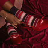 Red high-heeled shoes with a bow and red sheer striped socks on a red fabric background thumbnail