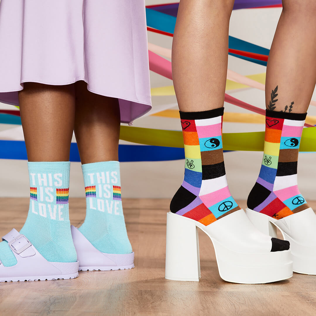Two pairs of feet wearing colorful socks with messages and designs, standing on a wooden floor.